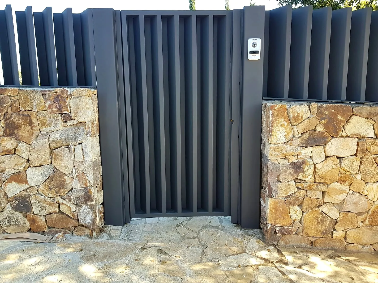 Puerta de lamas verticales entre muros de piedra